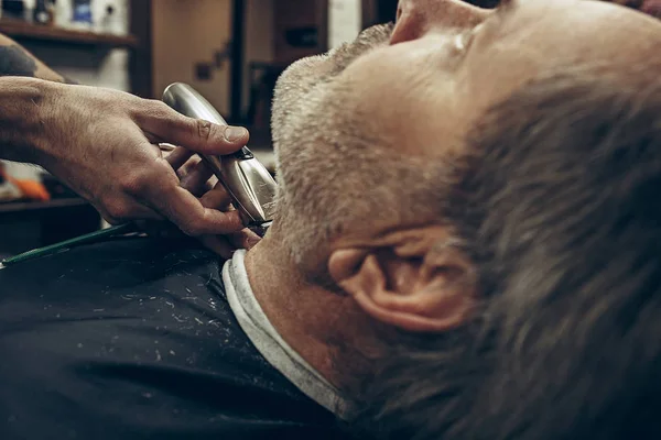 Close-up vista traseira lateral bonito homem caucasiano barbudo sênior recebendo barba grooming na barbearia moderna . — Fotografia de Stock