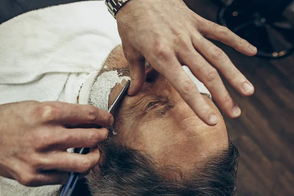 Close-up kant bovenaanzicht knappe senior bebaarde Kaukasische man krijgen baard verzorgen in moderne kapsalon. — Stockfoto
