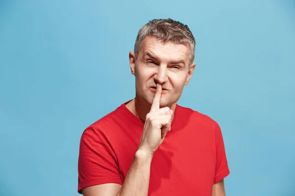 Der junge Mann flüstert ein Geheimnis hinter ihrer Hand vor blauem Hintergrund — Stockfoto