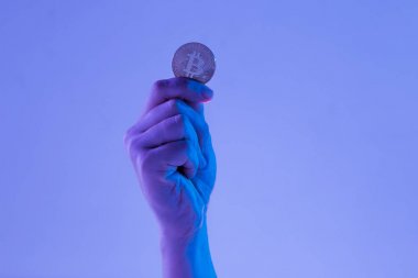 Male hand with golden bitcoin on blue background clipart