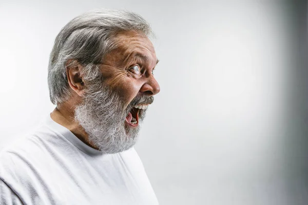 O homem irritado emocional sênior gritando no fundo do estúdio branco — Fotografia de Stock