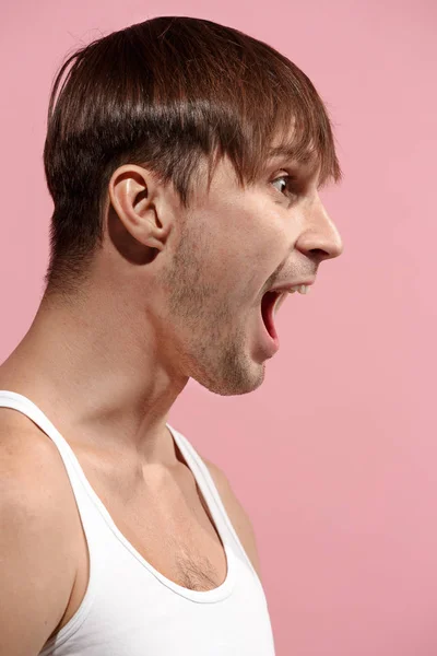 Молодий емоційно злий чоловік кричить на рожевому студійному фоні — стокове фото