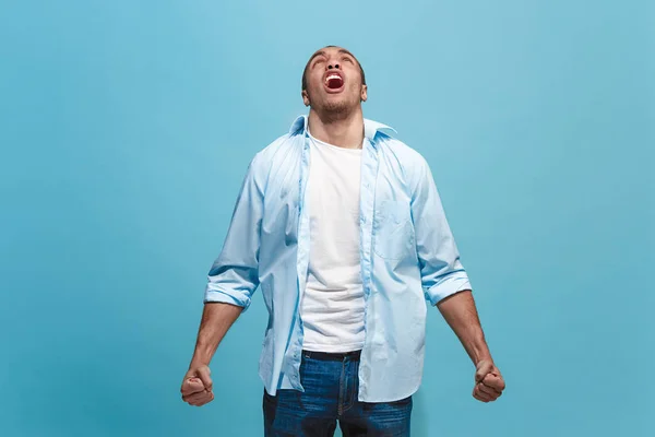 Молодой эмоциональный сердитый мужчина кричит на фоне синей студии — стоковое фото