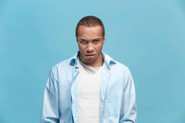 Молодой эмоциональный сердитый человек на фоне синей студии — стоковое фото