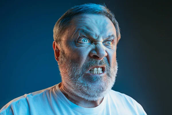 Старший эмоциональный сердитый мужчина кричит на фоне синей студии — стоковое фото