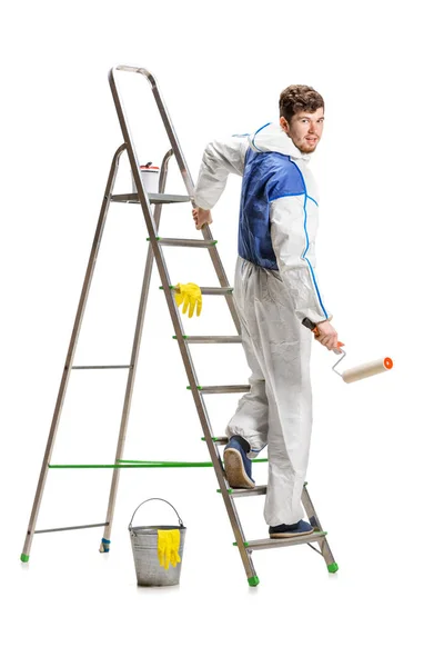 Young male decorator painting with a paint roller climbed a ladder isolated on white background. — Stock Photo, Image