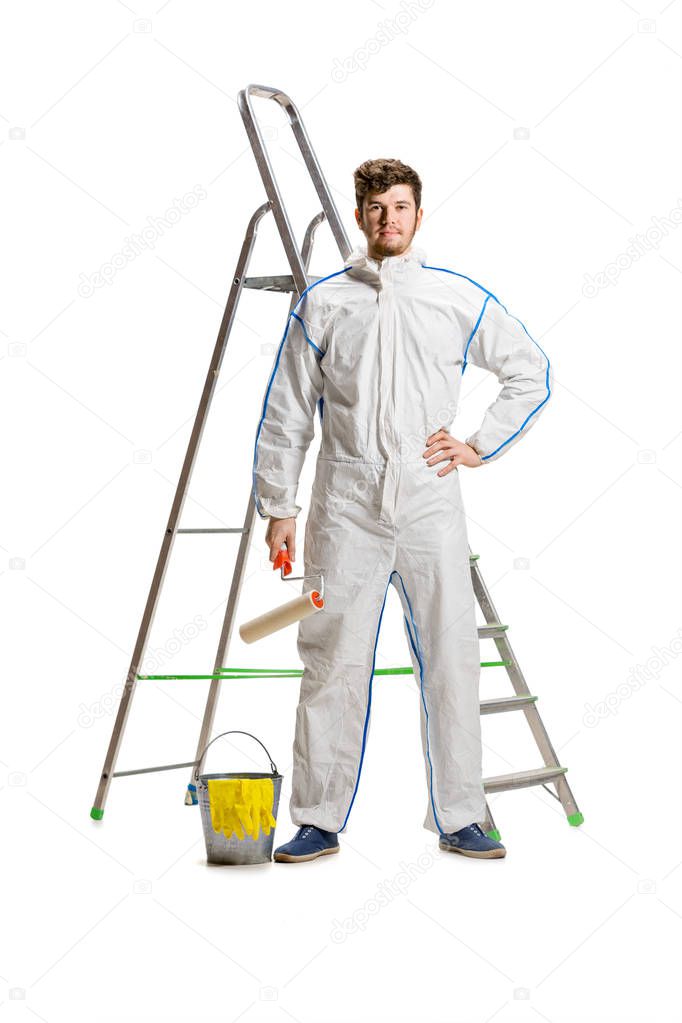Young male decorator painting with a paint roller climbed a ladder isolated on white background.