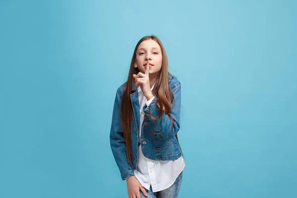 A jovem adolescente sussurrando um segredo atrás de sua mão sobre fundo azul — Fotografia de Stock