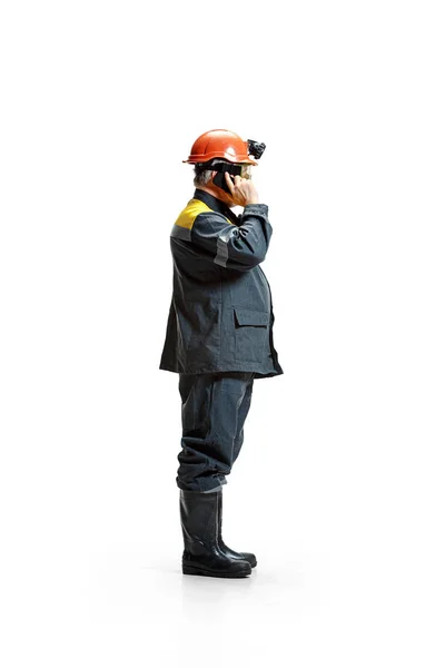The studio shot of serious senior bearded male miner standing in profile view at the camera with smartphone on a white background. — Stock Photo, Image