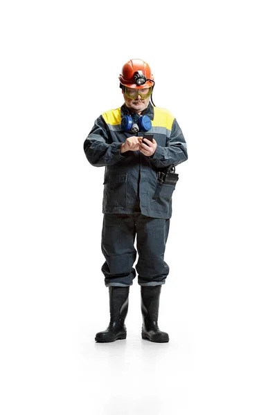 The studio shot of serious senior bearded male miner standing at the camera with smartphone on a white background. — Stock Photo, Image