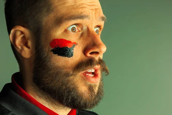 Portrait of a man with the flag of the Germany painted on him face.