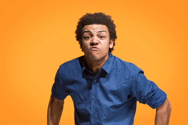 Молодой эмоциональный сердитый мужчина кричит на фоне оранжевой студии — стоковое фото