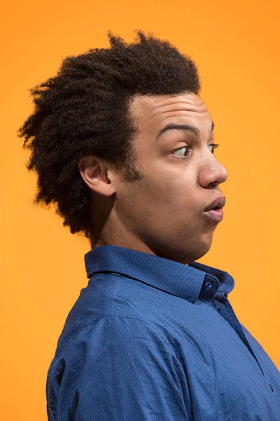 Молодой привлекательный мужчина выглядит удивленным изолированным от оранжевого — стоковое фото