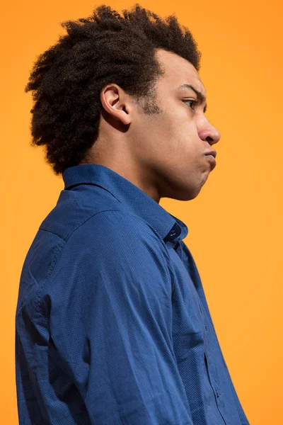 Молодой эмоциональный сердитый мужчина кричит на фоне оранжевой студии — стоковое фото