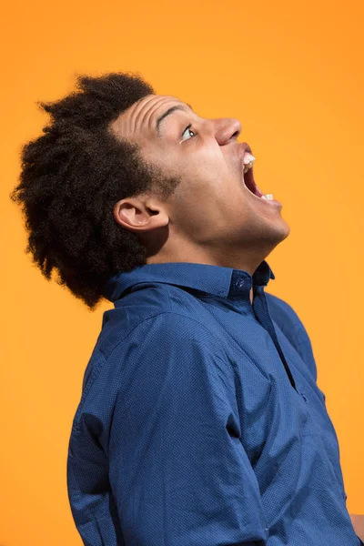 Der junge emotionale wütende Mann schreit auf orangefarbenem Studiohintergrund — Stockfoto