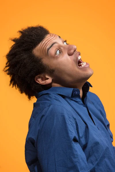 De jonge emotionele boos man schreeuwen op oranje studio achtergrond — Stockfoto