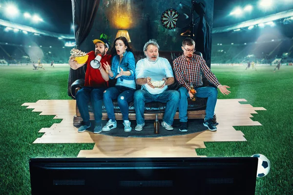 Ardent fans are sitting on the sofa and watching TV in the middle of a football field. — Stock Photo, Image