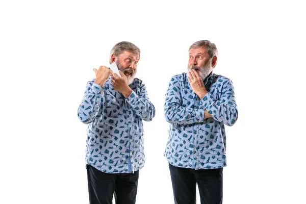 Homem sênior discutindo consigo mesmo no fundo do estúdio branco . — Fotografia de Stock