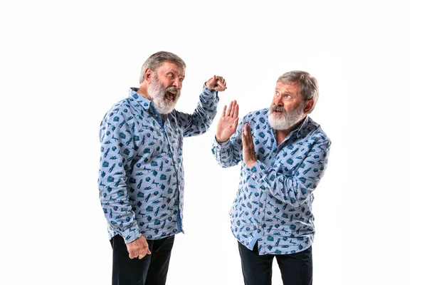 Hombre mayor discutiendo consigo mismo en el fondo del estudio blanco . — Foto de Stock