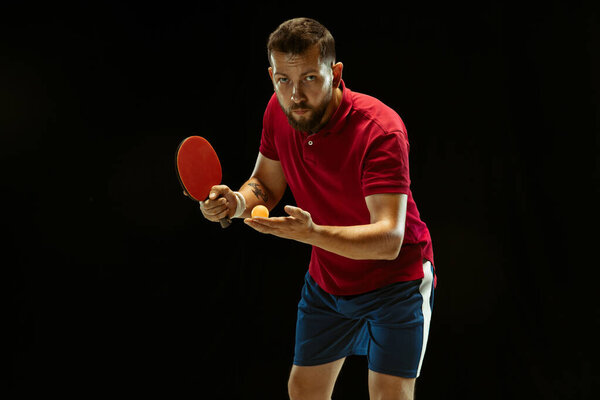 Young man playing table tennis on black studio background