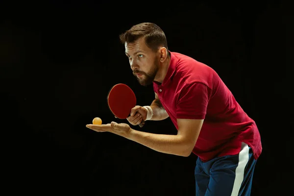 Young man playing table tennis on black studio background