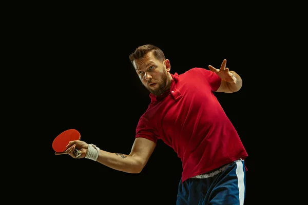 Young man playing table tennis on black studio background