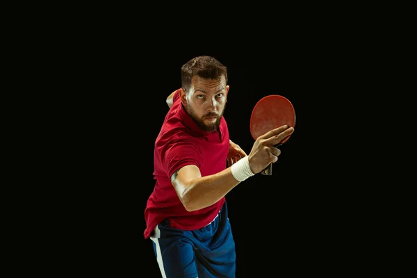 Young man playing table tennis on black studio background