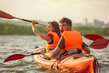 Mutlu çift nehirde kayak yapıyor, arka planda günbatımı var.