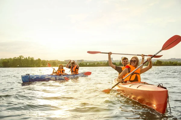 Lyckliga vänner kajakpaddling på floden med solnedgång på bakgrunden — Stockfoto