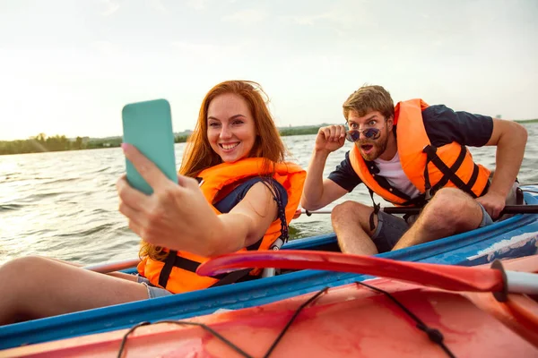 Happy couple kayaking on river with sunset on the background