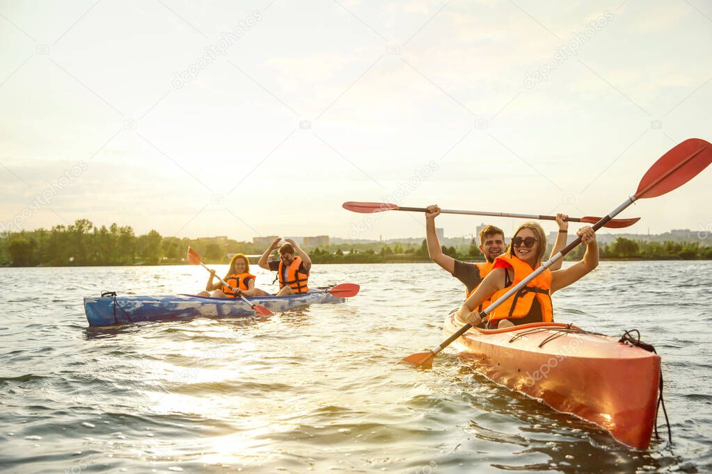 Happy friends kayaking on river with sunset on the background