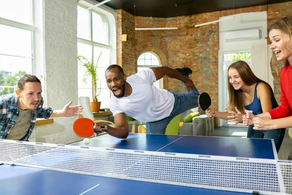 Jóvenes jugando al tenis de mesa en el lugar de trabajo, divirtiéndose —  Fotos de Stock