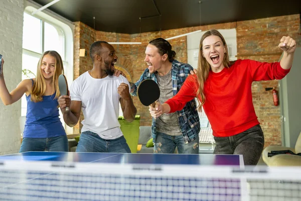 Jóvenes jugando al tenis de mesa en el lugar de trabajo, divirtiéndose —  Fotos de Stock