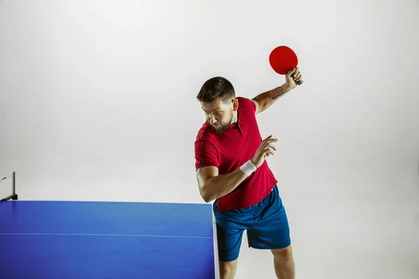 Young man playing table tennis on white studio background