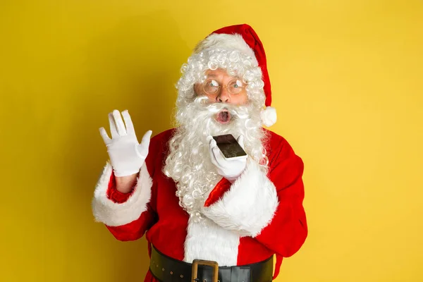 Weihnachtsmann mit modernen Gadgets isoliert auf gelbem Studiohintergrund — Stockfoto