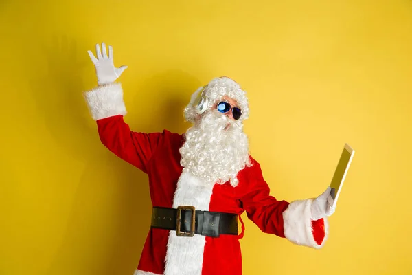Санта Клаус з сучасними гаджетами ізольовані на жовтому тлі студії — стокове фото