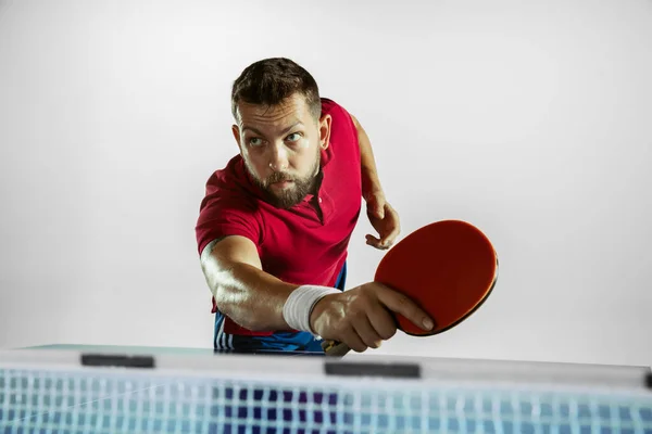 Young man playing table tennis on white studio background