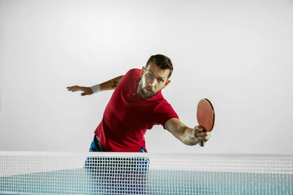 Young man playing table tennis on white studio background