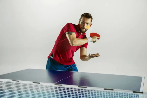 Young man playing table tennis on white studio background