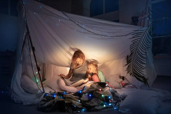 Anya és lánya egy sátorban ülnek, történeteket olvasnak a zseblámpával. — Stock Fotó