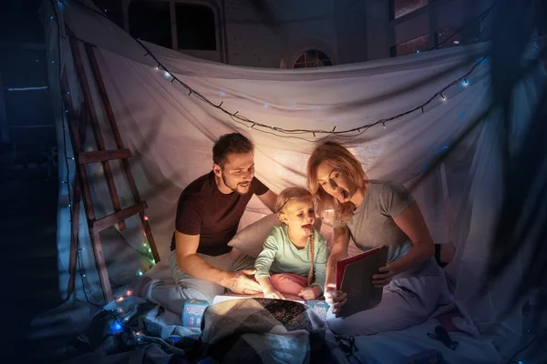 Family sitting in a teepee, having fun with the flashlight