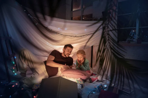 Pai e filha sentados em uma tenda, se divertindo com a lanterna — Fotografia de Stock
