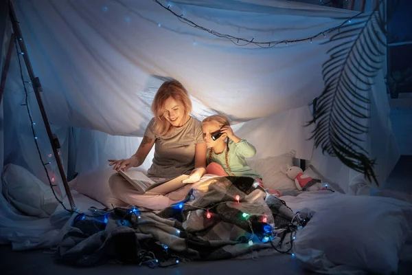 Anya és lánya egy sátorban ülnek, történeteket olvasnak a zseblámpával. — Stock Fotó