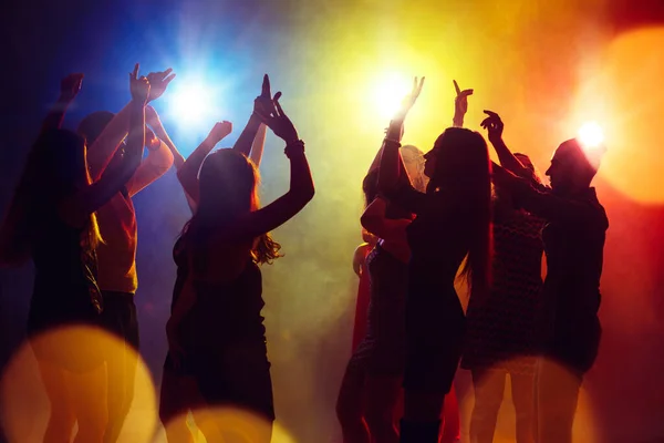 Una folla di persone in silhouette alza le mani contro la luce al neon colorata sullo sfondo del partito — Foto Stock