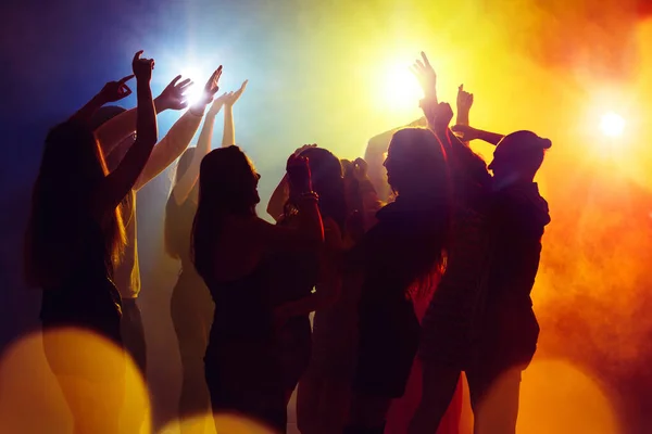 En skara människor i silhuett höjer händerna mot färgglada neon ljus på fest bakgrund — Stockfoto