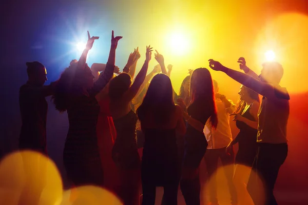 Толпа людей в силуэте поднимает руки на яркий неоновый свет на фоне вечеринки — стоковое фото