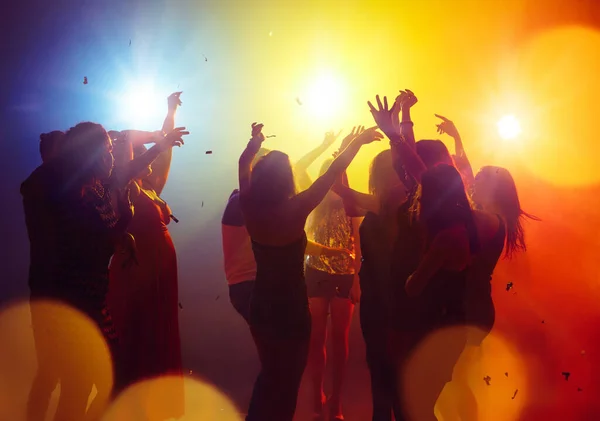 Una multitud de personas en silueta levanta las manos contra la colorida luz de neón en el fondo de la fiesta — Foto de Stock