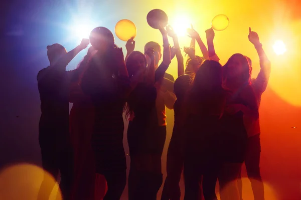A crowd of people in silhouette raises their hands against colorful neon light on party background — Stock Photo, Image