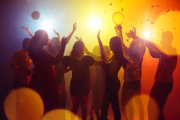 Una multitud de personas en silueta levanta las manos contra la colorida luz de neón en el fondo de la fiesta —  Fotos de Stock