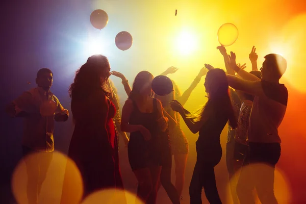 Una multitud de personas en silueta levanta las manos contra la colorida luz de neón en el fondo de la fiesta —  Fotos de Stock